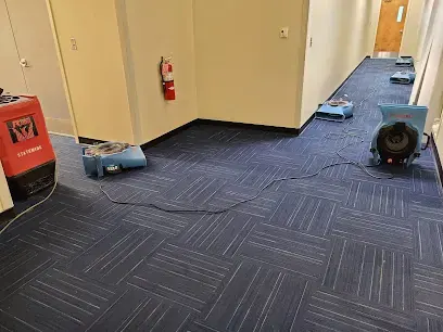 Air movers and a dehumidifier drying carpet tile in a Monroe Township office hallway