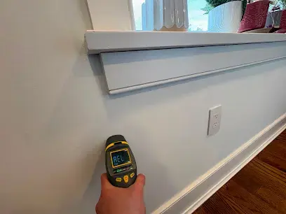 Technician checking a wall with a moisture reading meter during moisture mapping in a Monroe Township home
