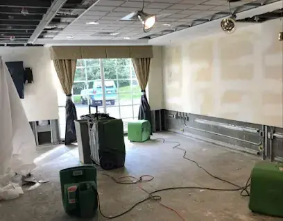 Dehumidifiers and air movers drying a large room with the lower walls opened during water damage restoration